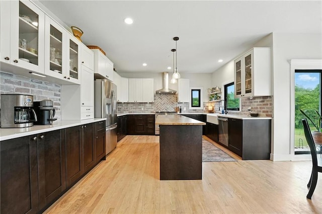 15376 Loring Rd, Bonner Springs, KS 66012 - kitchen with appliances with stainless steel finishes, wall chimney exhaust hood, light wood-style flooring, a kitchen island, and decorative backsplash