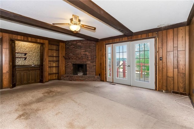 12417 Newton Ct, Grandview, MO 64030 - unfurnished living room with wood walls, carpet floors, beamed ceiling, a fireplace, and a ceiling fan