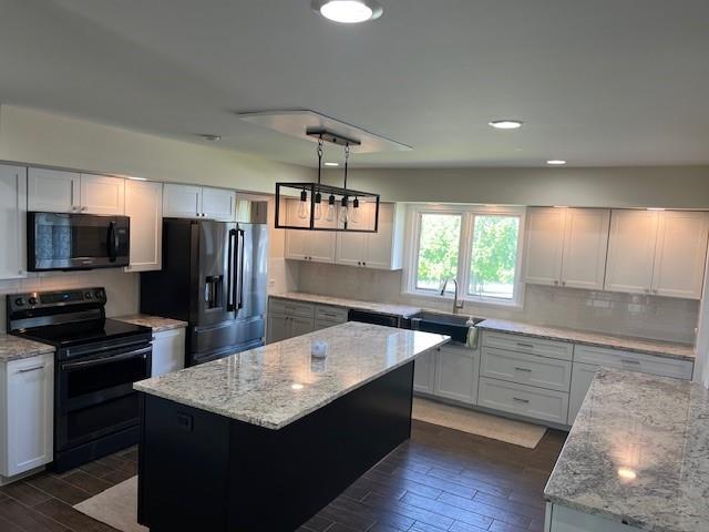 1901 NE River Ridge Rd, Saint Joseph, MO 64507 - kitchen featuring black appliances, a center island, dark wood-style flooring, decorative backsplash, and light stone countertops