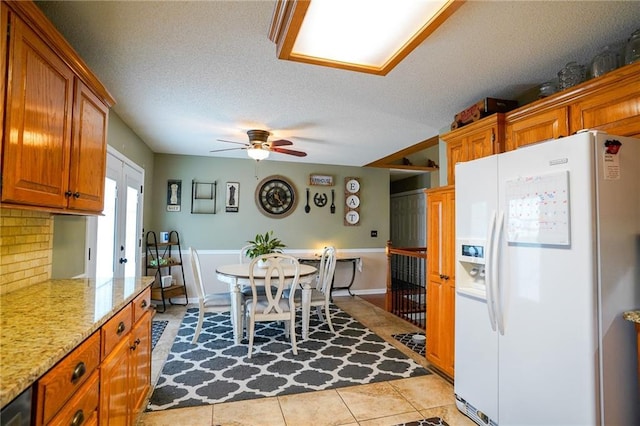 101 Shasta Daisy Dr, Smithville, MO 64089 - kitchen featuring white fridge with ice dispenser, ceiling fan, light tile patterned floors, brown cabinetry, and a textured ceiling