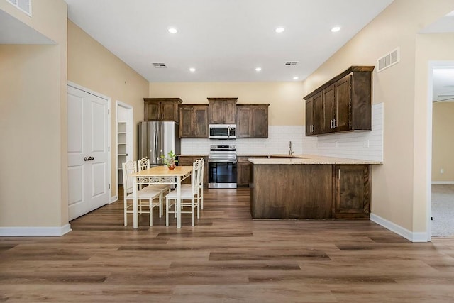 21119 E 8th St S, Independence, MO 64056 - kitchen featuring appliances with stainless steel finishes, dark brown cabinets, wood finished floors, tasteful backsplash, and light countertops