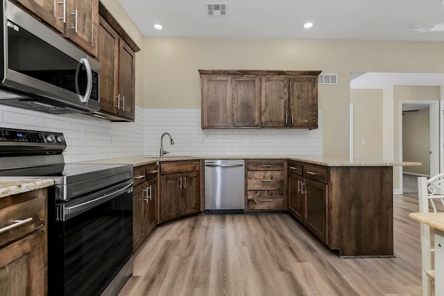 21119 E 8th St S, Independence, MO 64056 - kitchen featuring appliances with stainless steel finishes, a peninsula, light wood-type flooring, dark brown cabinets, and light stone counters