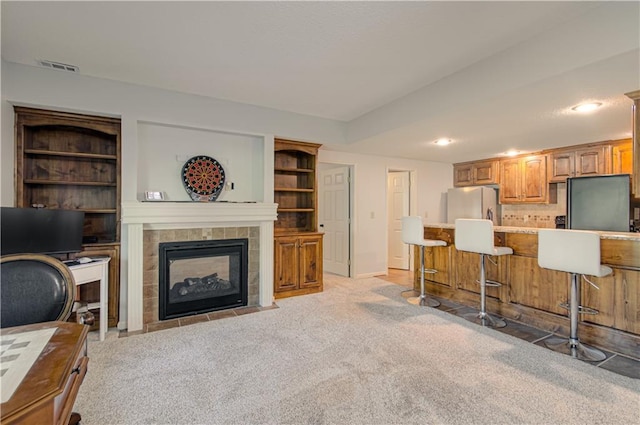 9624 N Arlington Ave, Kansas City, MO 64158 - kitchen featuring freestanding refrigerator, a kitchen bar, a tile fireplace, light carpet, and light countertops