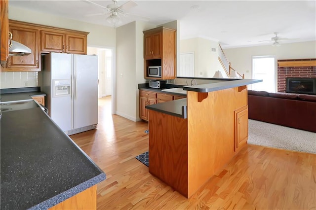 1503 Nottingham Dr, Warrensburg, MO 64093 - kitchen featuring ceiling fan, white refrigerator with ice dispenser, stainless steel microwave, under cabinet range hood, and a peninsula