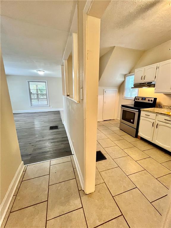 551 S Brookside Ave, Independence, MO 64053 - kitchen with stainless steel range with electric stovetop, white cabinetry, light tile patterned floors, plenty of natural light, and lofted ceiling