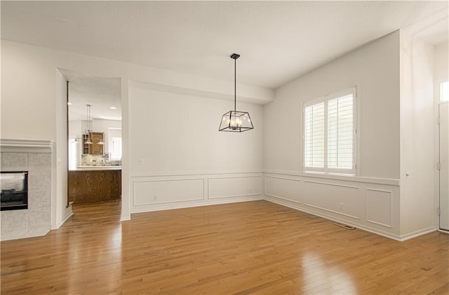 6306 W 128th St, Overland Park, KS 66209 - unfurnished dining area with wood finished floors, wainscoting, a chandelier, a tiled fireplace, and a decorative wall