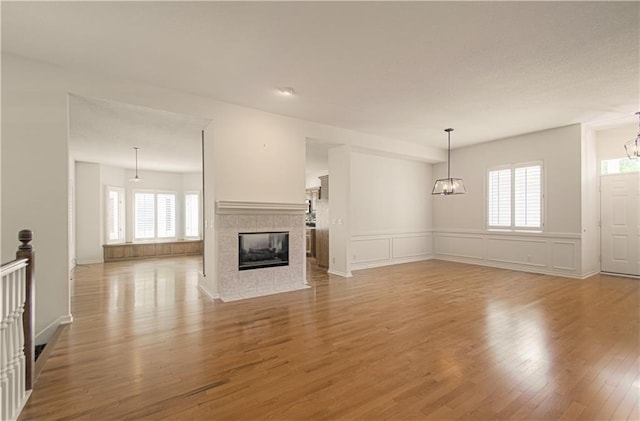 6306 W 128th St, Overland Park, KS 66209 - unfurnished living room featuring wood finished floors, a tile fireplace, wainscoting, a chandelier, and a decorative wall
