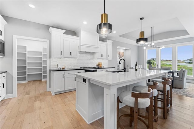 15837 El Monte St, Overland Park, KS 66224 - kitchen with white cabinets, tasteful backsplash, an island with sink, a breakfast bar, and premium range hood