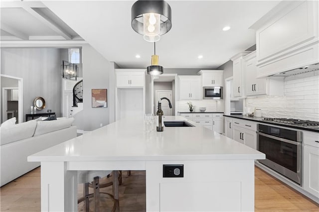 15837 El Monte St, Overland Park, KS 66224 - kitchen featuring stainless steel appliances, decorative backsplash, a large island with sink, white cabinets, and light wood finished floors