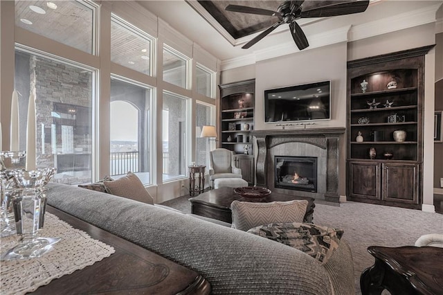 1217 Kingsland Cir, Raymore, MO 64083 - living area featuring a glass covered fireplace, ceiling fan, crown molding, built in shelves, and carpet