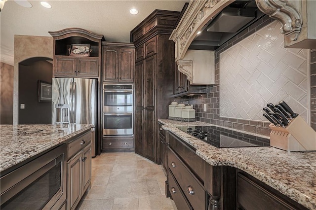 1217 Kingsland Cir, Raymore, MO 64083 - kitchen with appliances with stainless steel finishes, decorative backsplash, light stone counters, dark brown cabinets, and recessed lighting