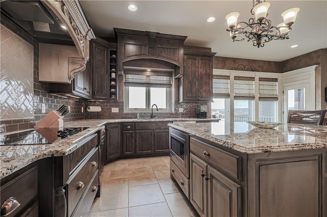 1217 Kingsland Cir, Raymore, MO 64083 - kitchen featuring black electric cooktop, stainless steel microwave, custom range hood, a chandelier, and backsplash