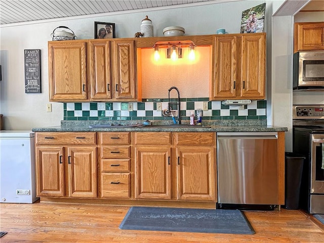 1607 S St, Lexington, MO 64067 - kitchen featuring appliances with stainless steel finishes, decorative backsplash, light wood-type flooring, and dark countertops