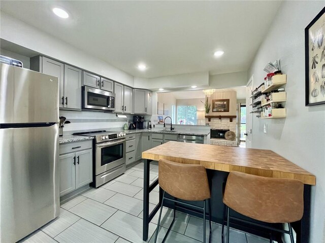 13148 S Brougham Dr, Olathe, KS 66062 - kitchen featuring stainless steel appliances, gray cabinets, a peninsula, backsplash, and a fireplace