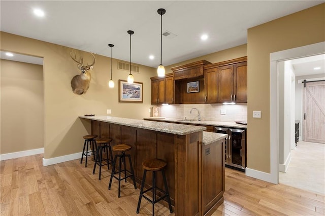 11717 S Barth Rd, Olathe, KS 66061 - kitchen with wine cooler, a kitchen bar, a barn door, light wood-style flooring, and a peninsula