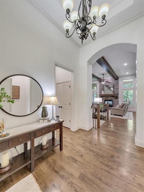 11599 S Carbondale St, Olathe, KS 66061 - entrance foyer with arched walkways, light wood-style flooring, a large fireplace, crown molding, and a chandelier