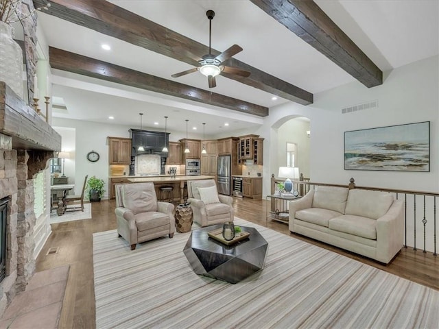 11599 S Carbondale St, Olathe, KS 66061 - living room featuring arched walkways, ceiling fan, light wood-type flooring, a stone fireplace, and beam ceiling