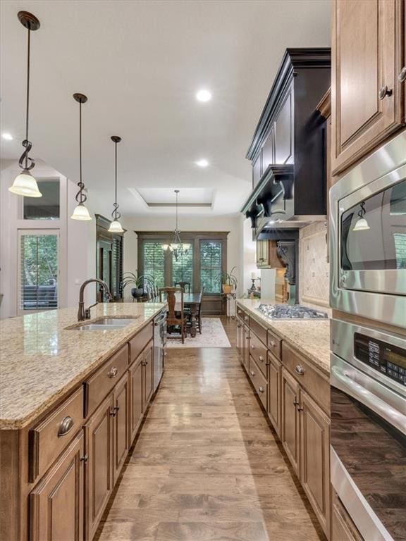 11599 S Carbondale St, Olathe, KS 66061 - kitchen with appliances with stainless steel finishes, a raised ceiling, light wood finished floors, light stone counters, and hanging light fixtures