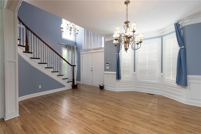 8620 N Eastern Ave, Kansas City, MO 64157 - unfurnished dining area featuring a chandelier, wood finished floors, stairs, wainscoting, and a decorative wall