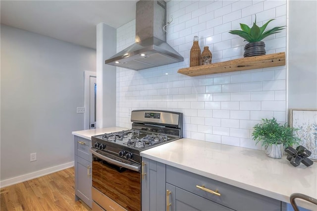 11417 Applewood Dr, Kansas City, MO 64134 - kitchen with wall chimney range hood, stainless steel range with gas stovetop, gray cabinets, backsplash, and light wood finished floors