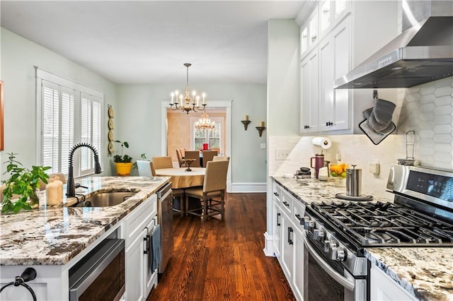 3215 Windsor Ave, Kansas City, MO 64123 - kitchen with stainless steel appliances, wall chimney range hood, dark wood finished floors, a chandelier, and white cabinetry