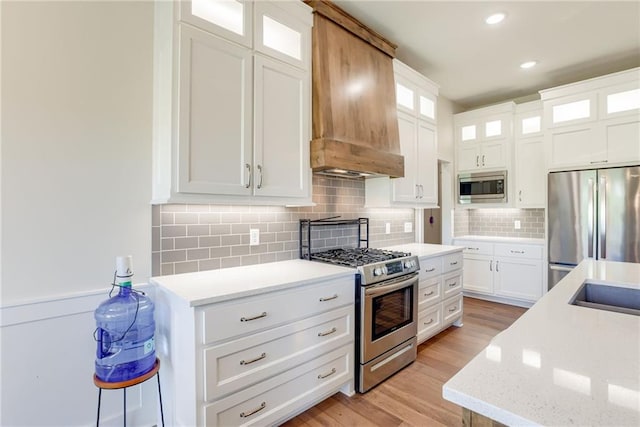 12750 Larkspur Ln, Platte City, MO 64079 - kitchen featuring stainless steel appliances, premium range hood, light wood-style flooring, tasteful backsplash, and white cabinetry