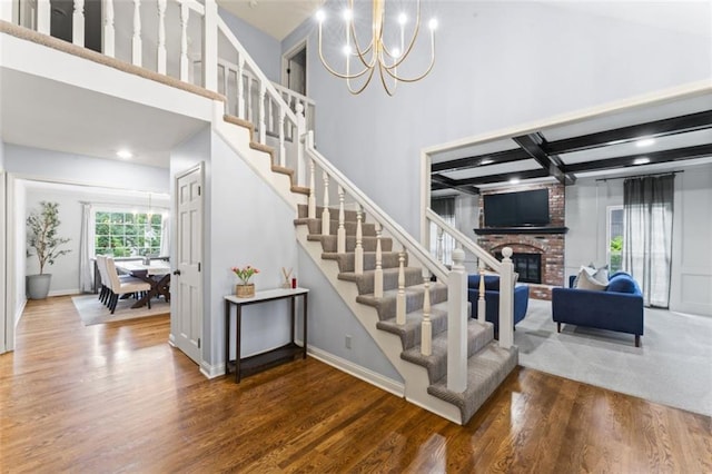 2405 W 124th St, Leawood, KS 66209 - staircase with a chandelier, wood finished floors, a fireplace, a towering ceiling, and beamed ceiling