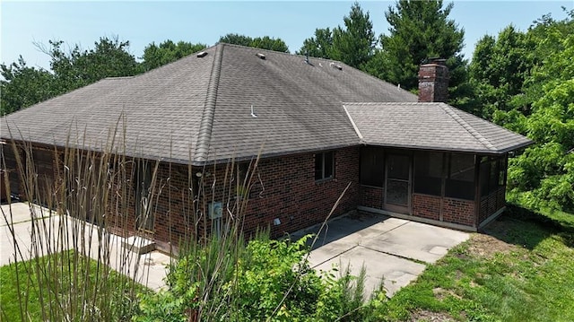 3111 N 35th St, Saint Joseph, MO 64506 - back of house with a sunroom, a shingled roof, a chimney, a patio area, and brick siding