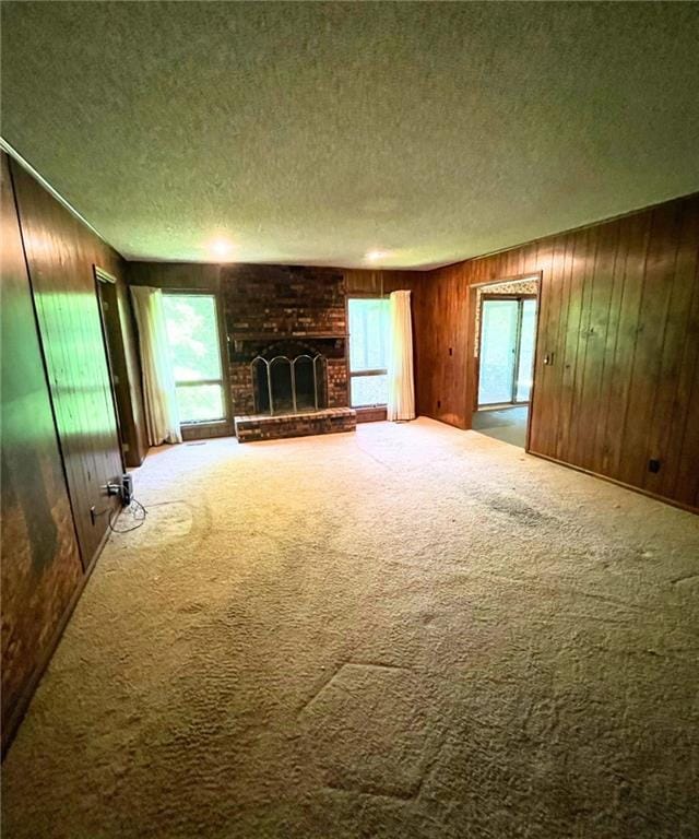 3111 N 35th St, Saint Joseph, MO 64506 - unfurnished living room featuring a textured ceiling, carpet flooring, healthy amount of natural light, a fireplace, and wood walls