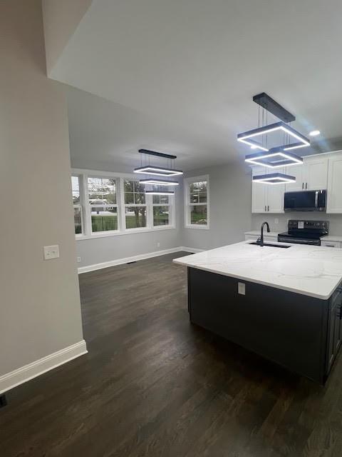 26433 W 144th Ter, Olathe, KS 66061 - kitchen with black / electric stove, stainless steel microwave, light stone counters, a center island with sink, and white cabinets