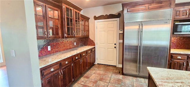 789 Maple Rd, Uniontown, KS 66779 - kitchen with appliances with stainless steel finishes, decorative backsplash, glass insert cabinets, light stone countertops, and dark brown cabinets