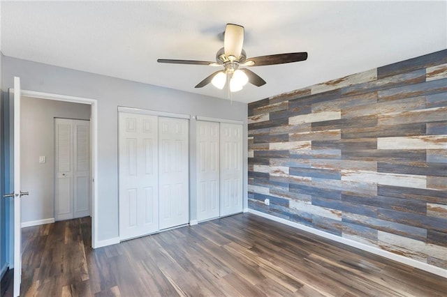 10017 W 95th St, Overland Park, KS 66212 - unfurnished bedroom with an accent wall, wood walls, wood finished floors, multiple closets, and a ceiling fan