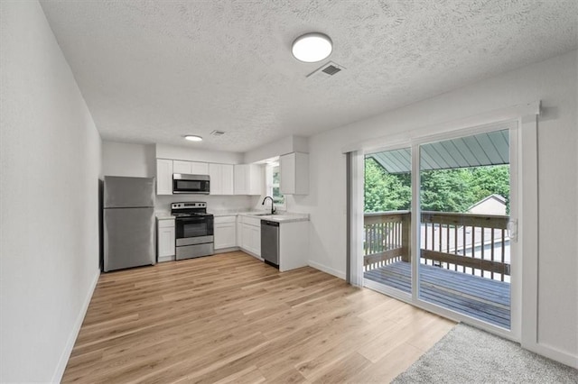 1000 Twin Oaks Ter, Harrisonville, MO 64701 - kitchen featuring stainless steel appliances, light countertops, a textured ceiling, light wood finished floors, and white cabinetry