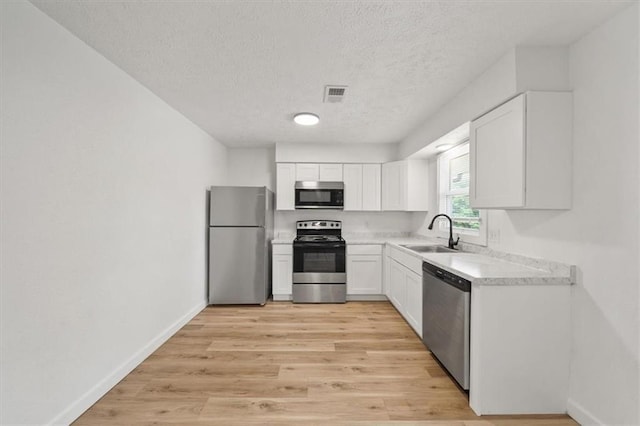 1000 Twin Oaks Ter, Harrisonville, MO 64701 - kitchen featuring appliances with stainless steel finishes, a textured ceiling, white cabinetry, light countertops, and light wood-style flooring