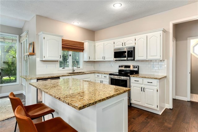 14010 Ash St, Overland Park, KS 66224 - kitchen featuring stainless steel appliances, a kitchen breakfast bar, white cabinets, light stone countertops, and a textured ceiling
