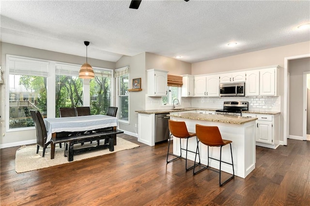 14010 Ash St, Overland Park, KS 66224 - kitchen featuring appliances with stainless steel finishes, white cabinetry, backsplash, a kitchen island, and dark wood finished floors