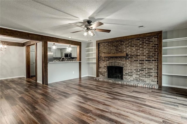 10734 Glenwood St Unit A, Overland Park, KS 66211 - unfurnished living room featuring dark wood-style floors, a ceiling fan, a fireplace, a textured ceiling, and a chandelier