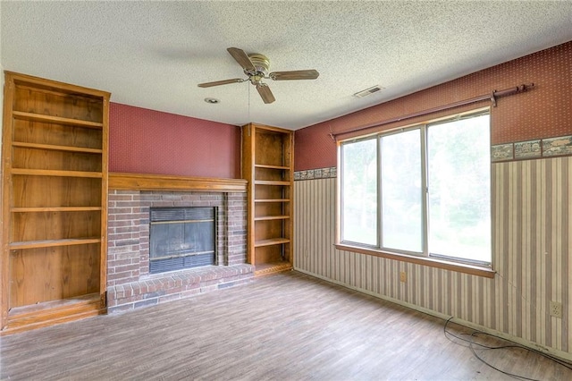 18120 E 25th Ter, Independence, MO 64057 - unfurnished living room featuring wallpapered walls, wood finished floors, a textured ceiling, a ceiling fan, and a fireplace