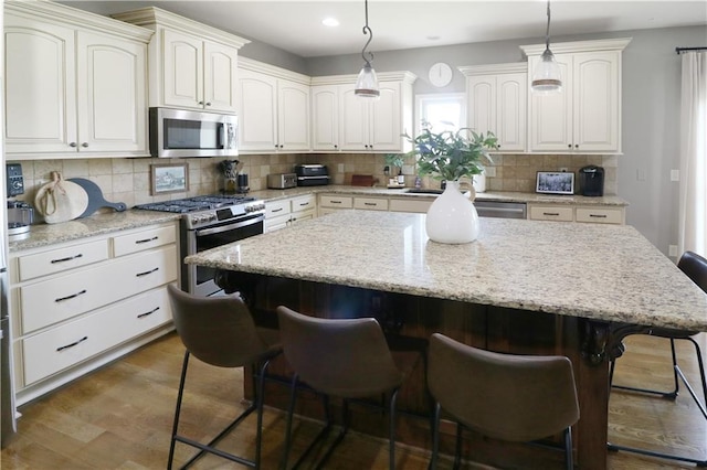 1216 Hillmann Ln, Warrensburg, MO 64093 - kitchen featuring appliances with stainless steel finishes, a kitchen bar, decorative backsplash, a kitchen island, and hanging light fixtures