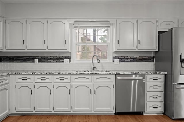 12343 Pinehurst Dr, Kansas City, KS 66109 - kitchen featuring appliances with stainless steel finishes, light stone countertops, white cabinetry, decorative backsplash, and wood finished floors
