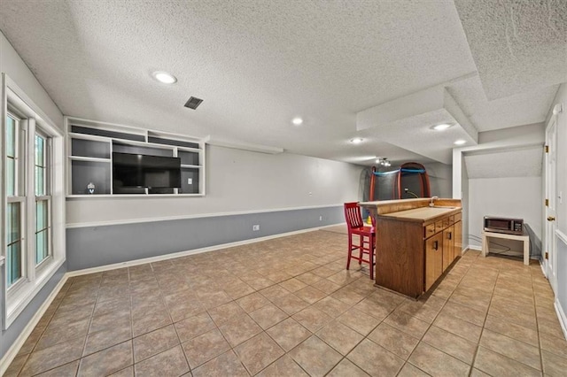 10601 Reeder St, Overland Park, KS 66214 - kitchen featuring a textured ceiling, brown cabinetry, recessed lighting, and a kitchen bar