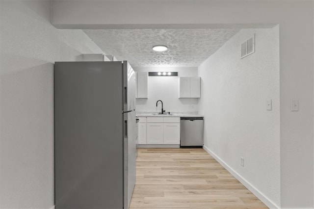 904 Twin Oaks Ter, Harrisonville, MO 64701 - kitchen with stainless steel appliances, light countertops, a textured wall, white cabinets, and light wood-style floors