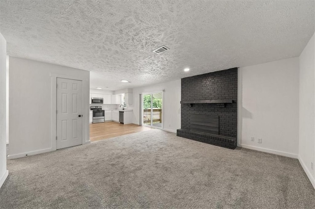 904 Twin Oaks Ter, Harrisonville, MO 64701 - unfurnished living room featuring a brick fireplace, light colored carpet, a textured ceiling, and recessed lighting