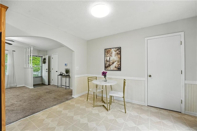 1303 SW Mission Pl, Lees Summit, MO 64081 - dining space featuring arched walkways, light colored carpet, a wainscoted wall, light floors, and a textured ceiling