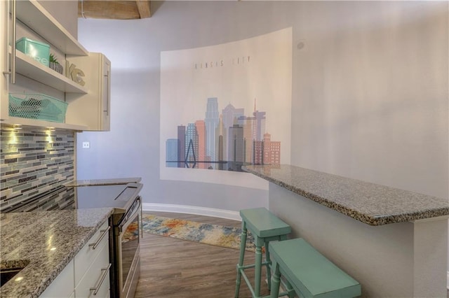 308 W 8th St Unit 420, Kansas City, MO 64105 - kitchen with decorative backsplash, dark wood finished floors, a kitchen bar, electric stove, and light stone counters