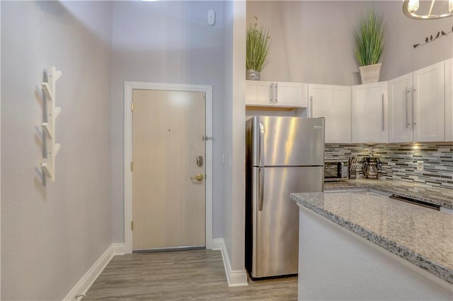 308 W 8th St Unit 420, Kansas City, MO 64105 - kitchen featuring freestanding refrigerator, tasteful backsplash, white cabinets, light wood finished floors, and light stone countertops