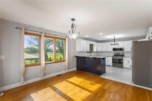 1125 S Mulberry St, Ottawa, KS 66067 - kitchen featuring appliances with stainless steel finishes, a peninsula, a chandelier, white cabinets, and light wood finished floors