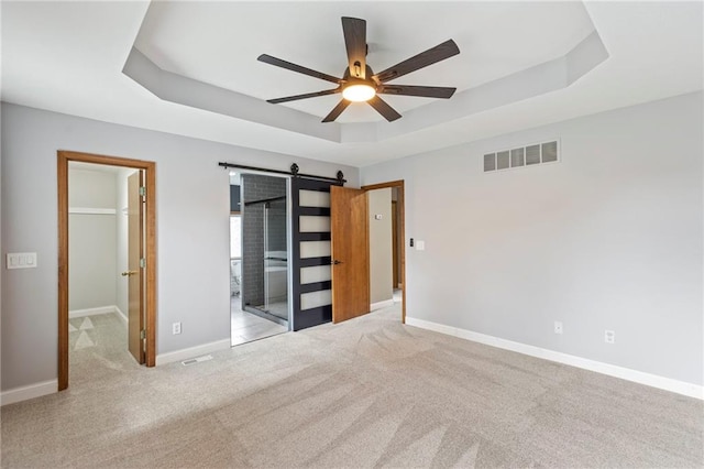 1125 S Mulberry St, Ottawa, KS 66067 - unfurnished bedroom featuring a raised ceiling, a barn door, carpet flooring, a spacious closet, and a ceiling fan