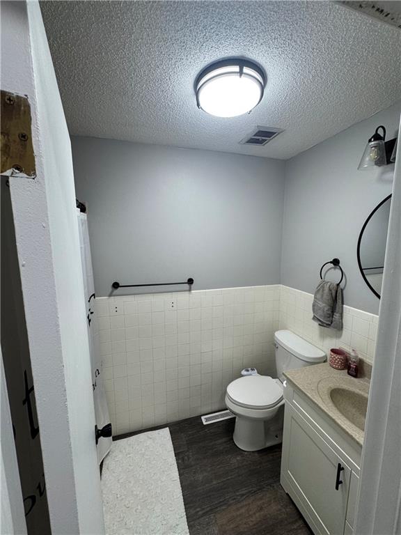 109 W 3rd St, Stanberry, MO 64489 - full bath with vanity, wood finished floors, a wainscoted wall, tile walls, and a textured ceiling