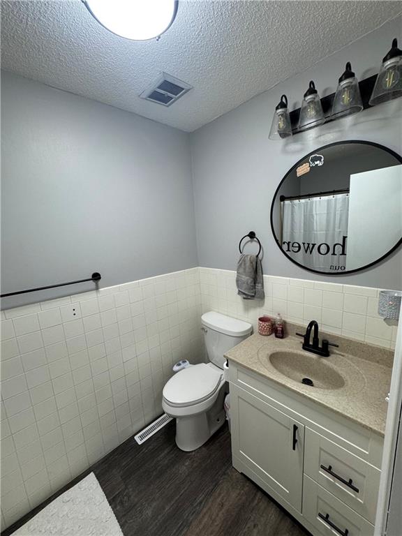 109 W 3rd St, Stanberry, MO 64489 - full bath featuring wood finished floors, vanity, a textured ceiling, tile walls, and a wainscoted wall